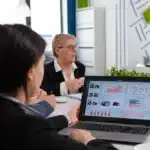 Profissionais analisando um dashboard de vendas em um laptop durante reunião.